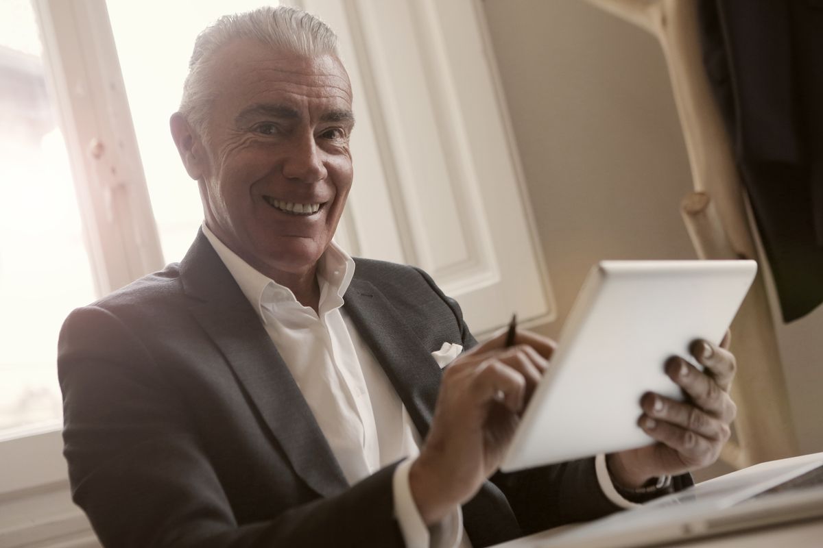 Hombre mayor sonriendo con confianza mientras usa una tablet